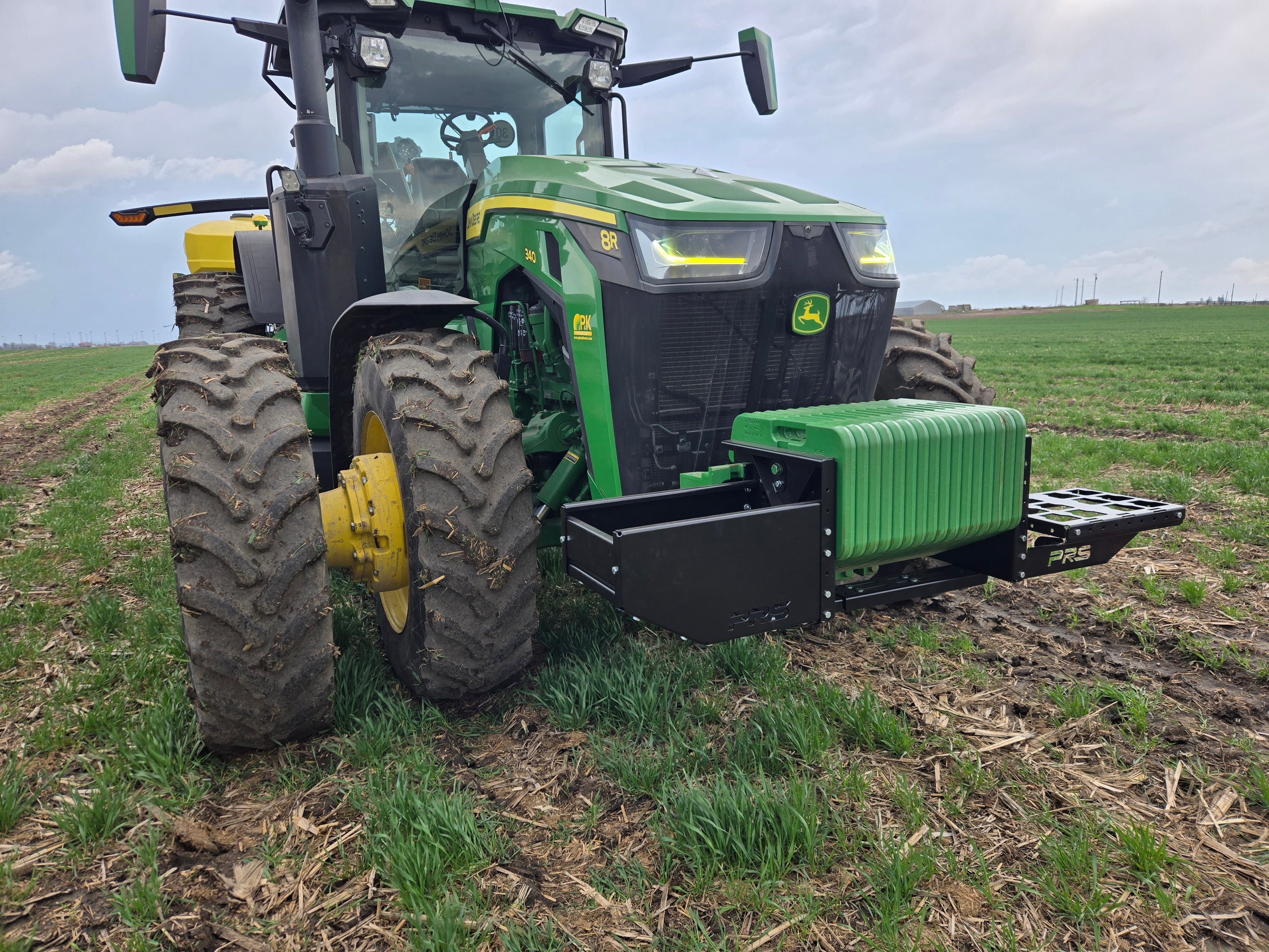 Green John Deere tractor in a field with a cloudy sky.