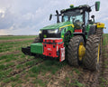 Green tractor with a red attachment in a field on a cloudy day